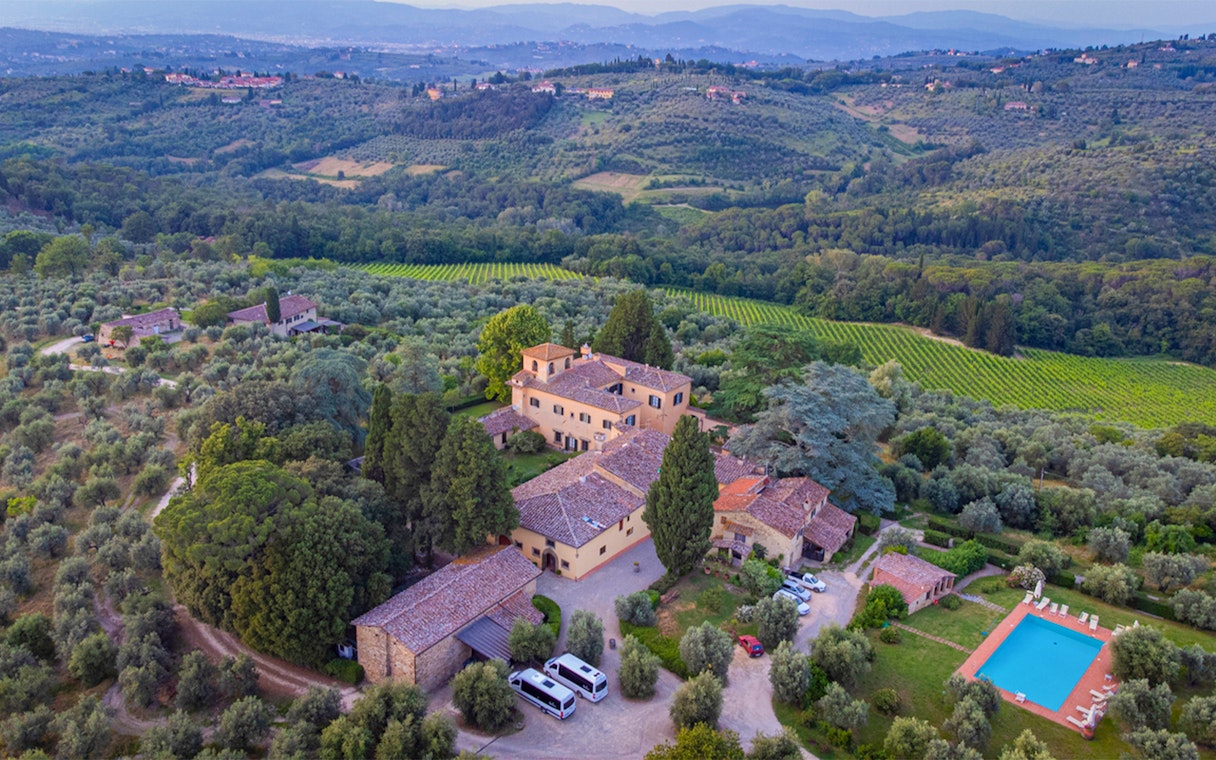 Aerial view of a Tuscan villa surrounded by vineyards and olive groves, part of the Tuscany Grand Tour.
