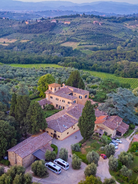 Aerial view of a Tuscan villa surrounded by vineyards and olive groves, part of the Tuscany Grand Tour.