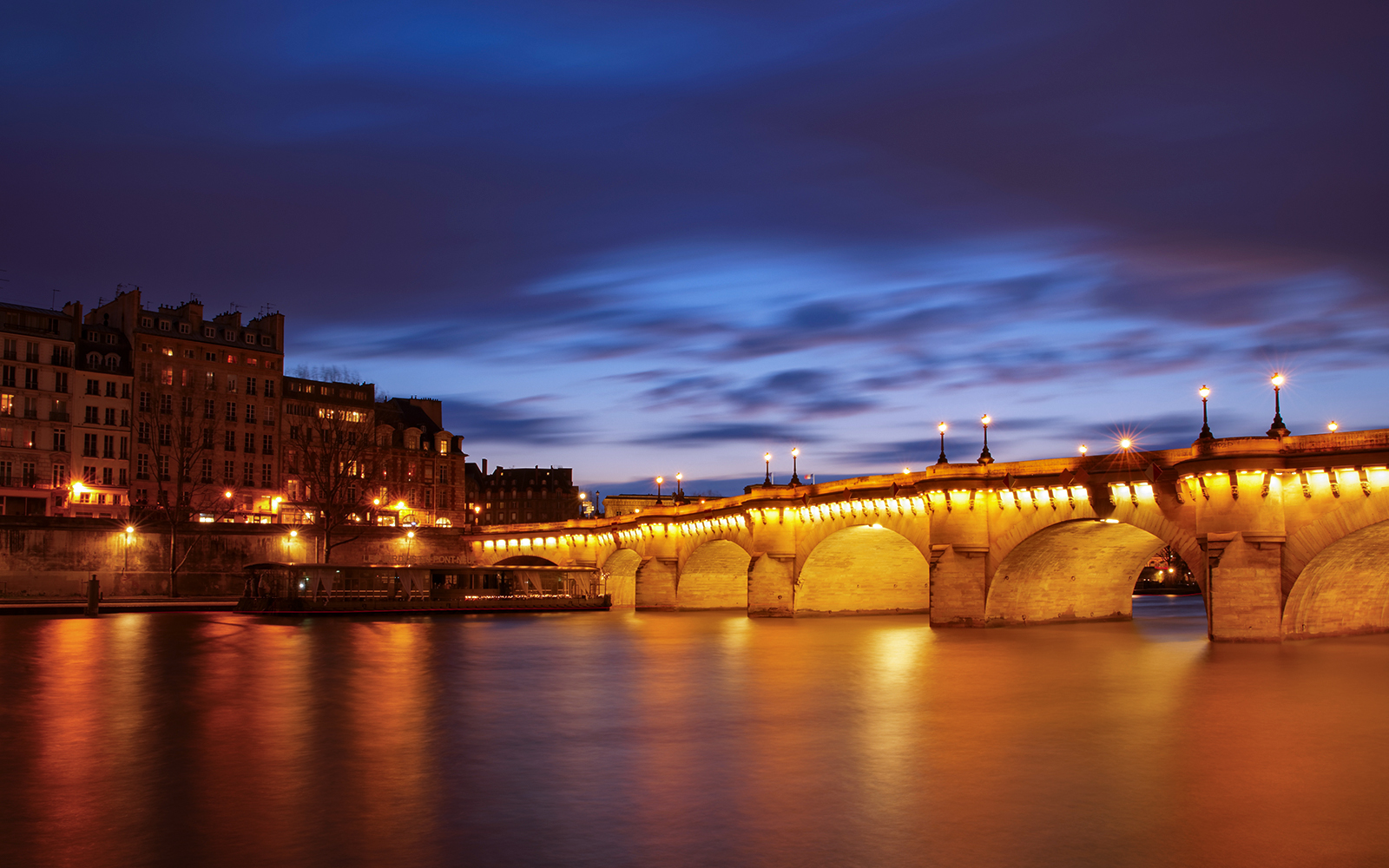 Pont Neuf illuminated at night, viewed from a river cruise in Paris.