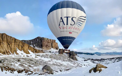 Hot air balloon over snowy Ihlara Canyon landscape at sunrise, Cappadocia.