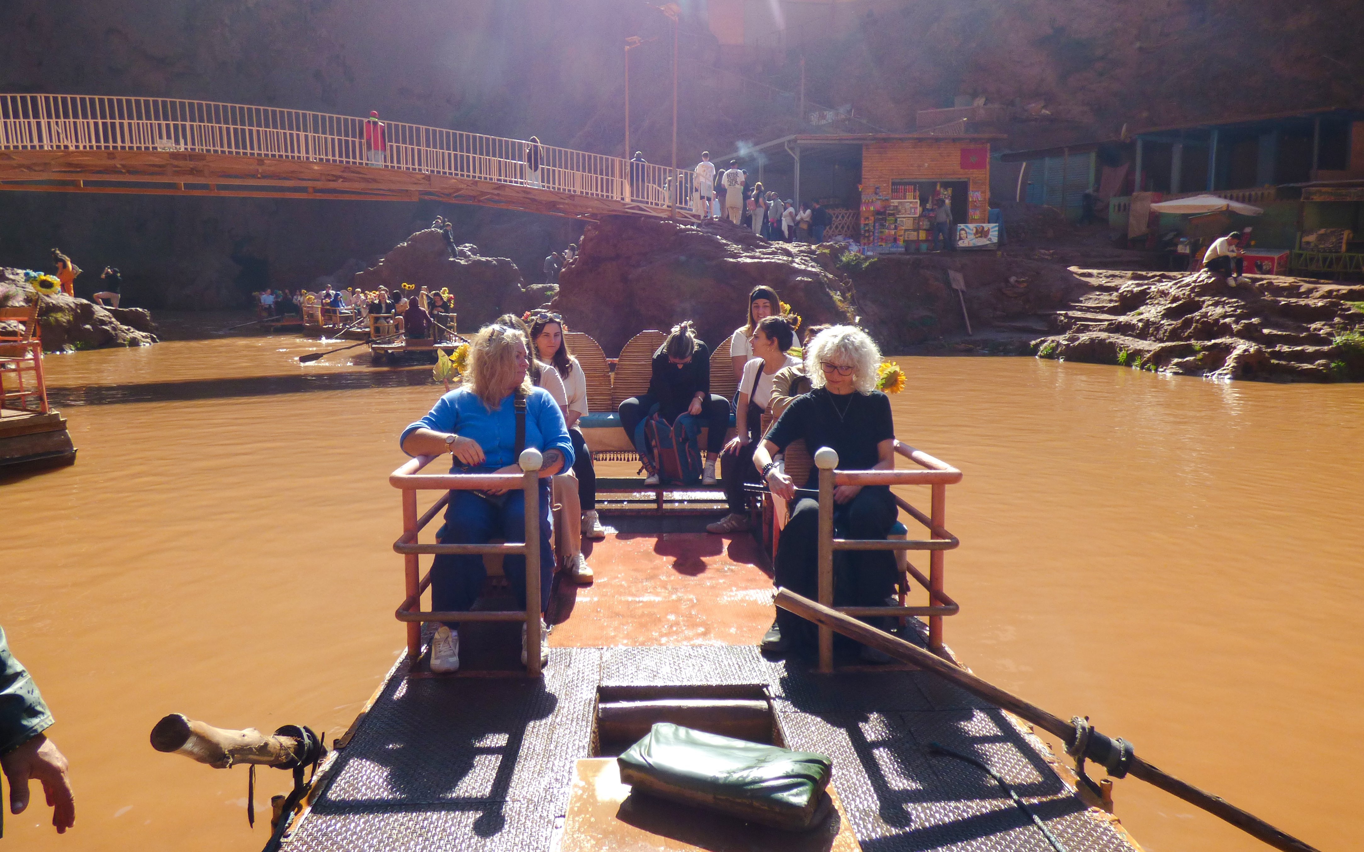 Tourists enjoying a boat ride at Ouzoud Waterfalls, Morocco, with a scenic bridge in the background.