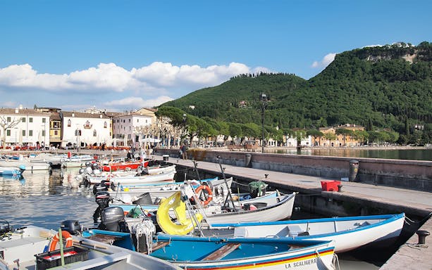 Boats docked at a marina with a view of Lake Garda and surrounding hills.