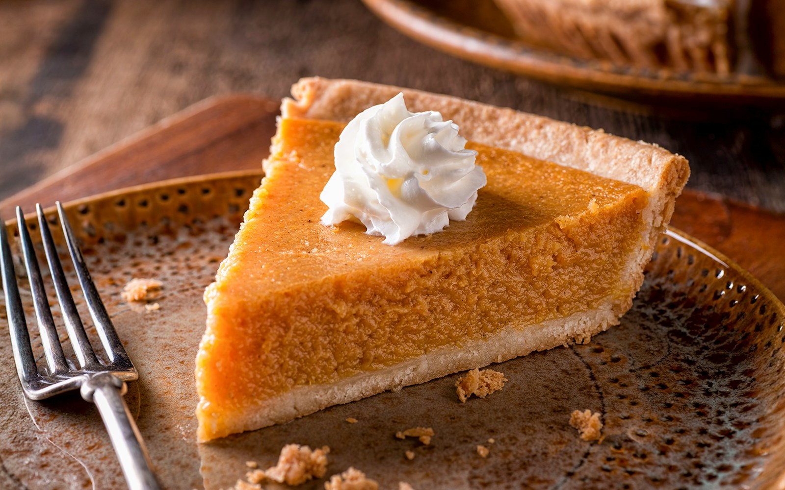 Slice of pumpkin pie topped with whipped cream on a plate with a fork.