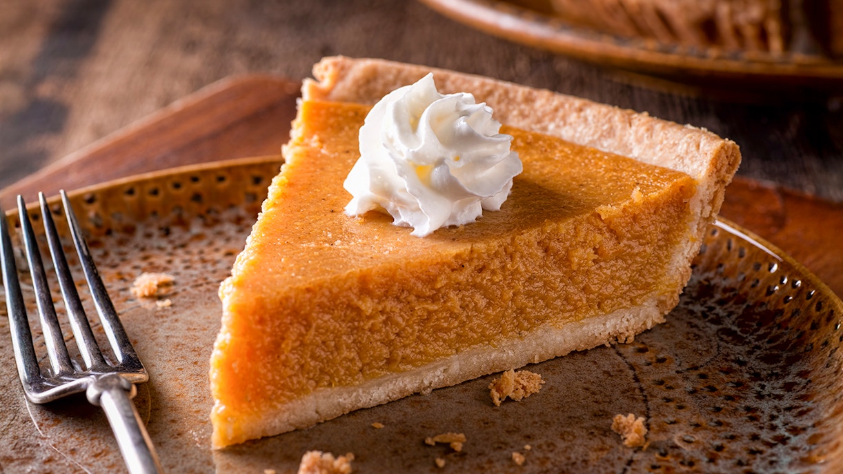 Slice of pumpkin pie topped with whipped cream on a plate with a fork.