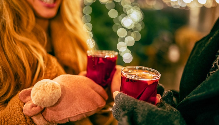 Two people holding glasses of mulled wine at a festive market.