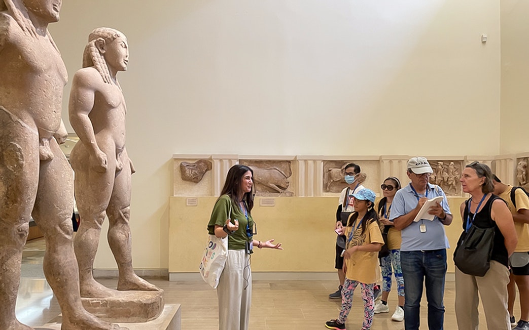 Tour guide explaining ancient statues to visitors inside Delphi Museum.