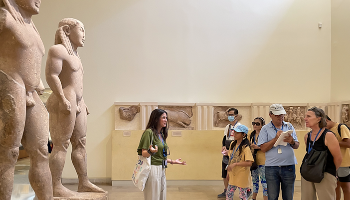 Tour guide explaining ancient statues to visitors inside Delphi Museum.