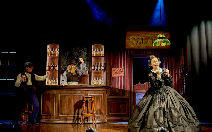 Saloon scene from "Oh Mary!" with actors in period costumes, one behind the bar, another holding a mug.