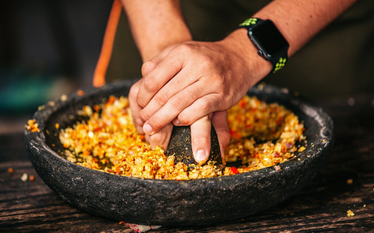 Hands grinding spices in a stone mortar during a cooking class in Canggu, Bali.