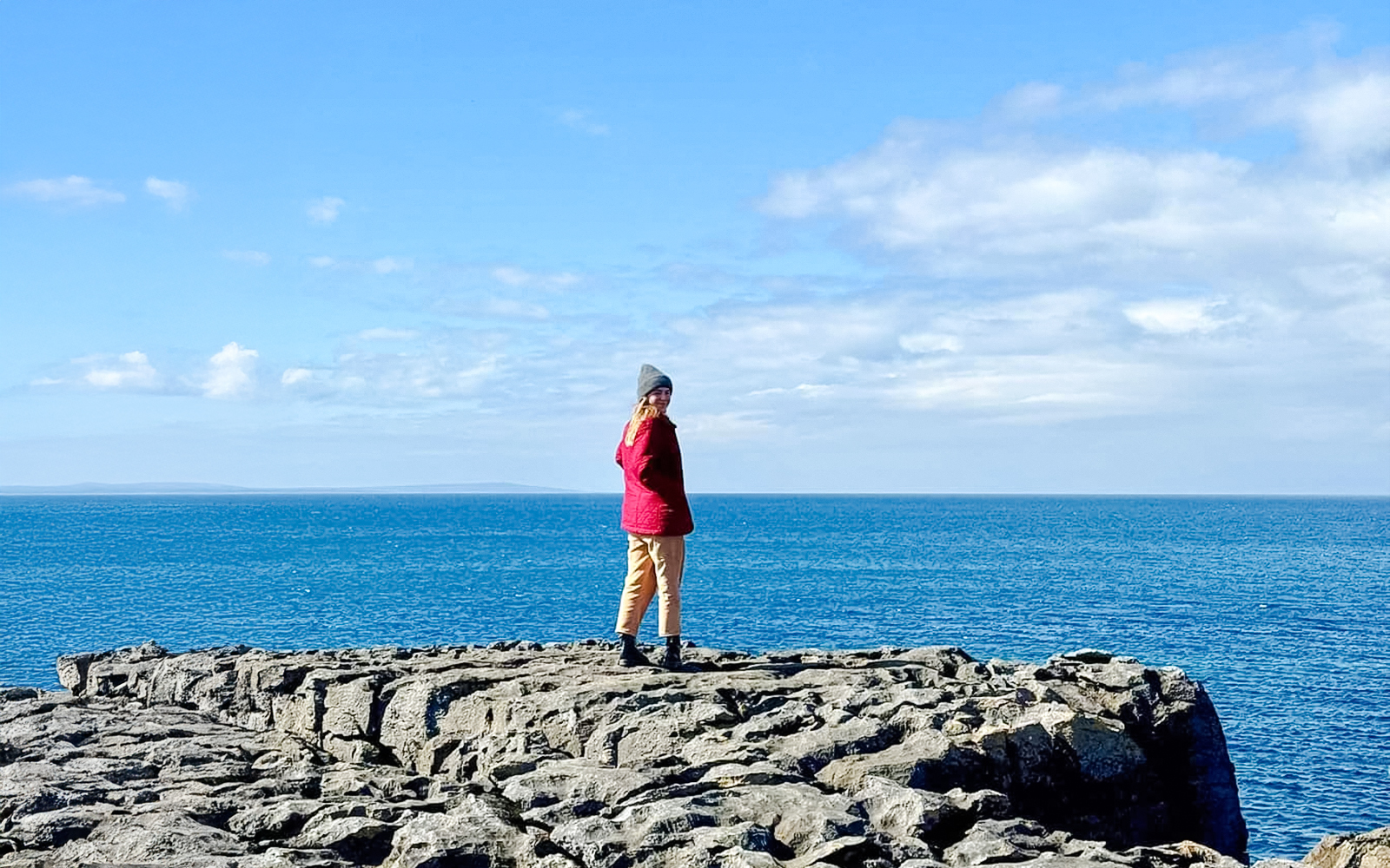 Person standing on limestone rocks overlooking the ocean in The Burren, Ireland.