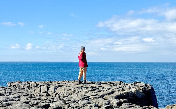 Person standing on limestone rocks overlooking the ocean in The Burren, Ireland.