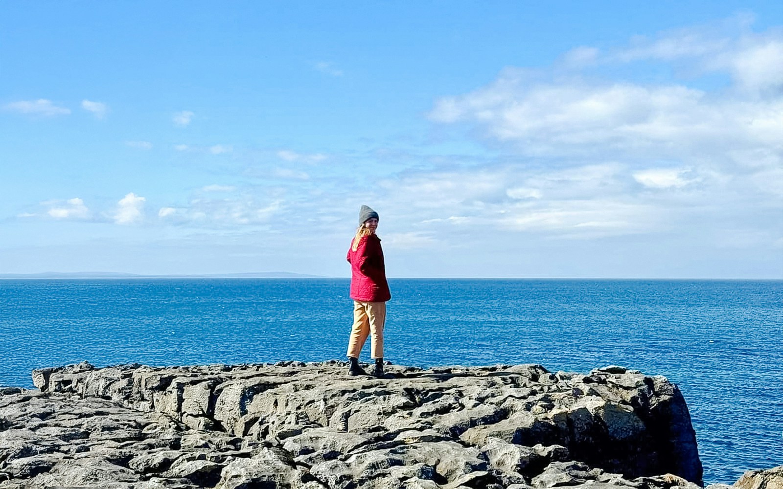 Person standing on limestone rocks overlooking the ocean in The Burren, Ireland.