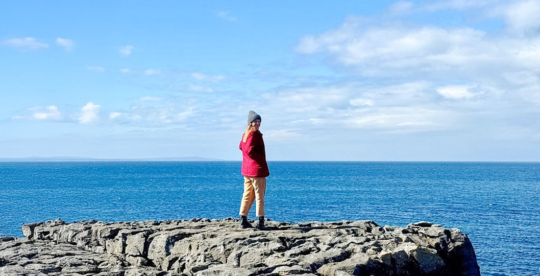 Person standing on limestone rocks overlooking the ocean in The Burren, Ireland.