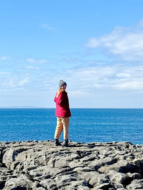 Person standing on limestone rocks overlooking the ocean in The Burren, Ireland.