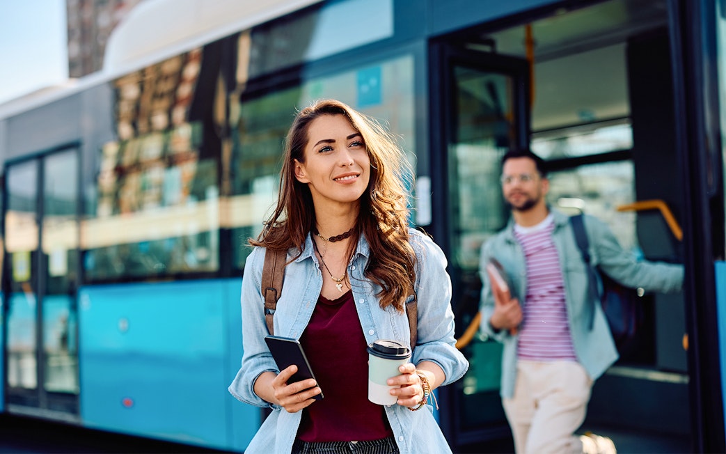People disembarking from a bus in Giverny, France, holding coffee and phones.