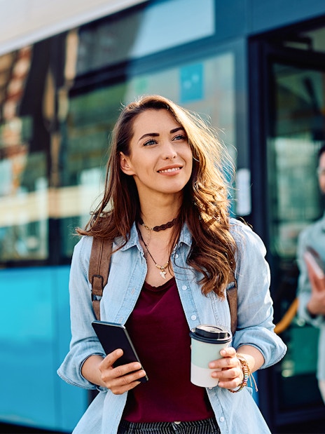 People disembarking from a bus in Giverny, France, holding coffee and phones.