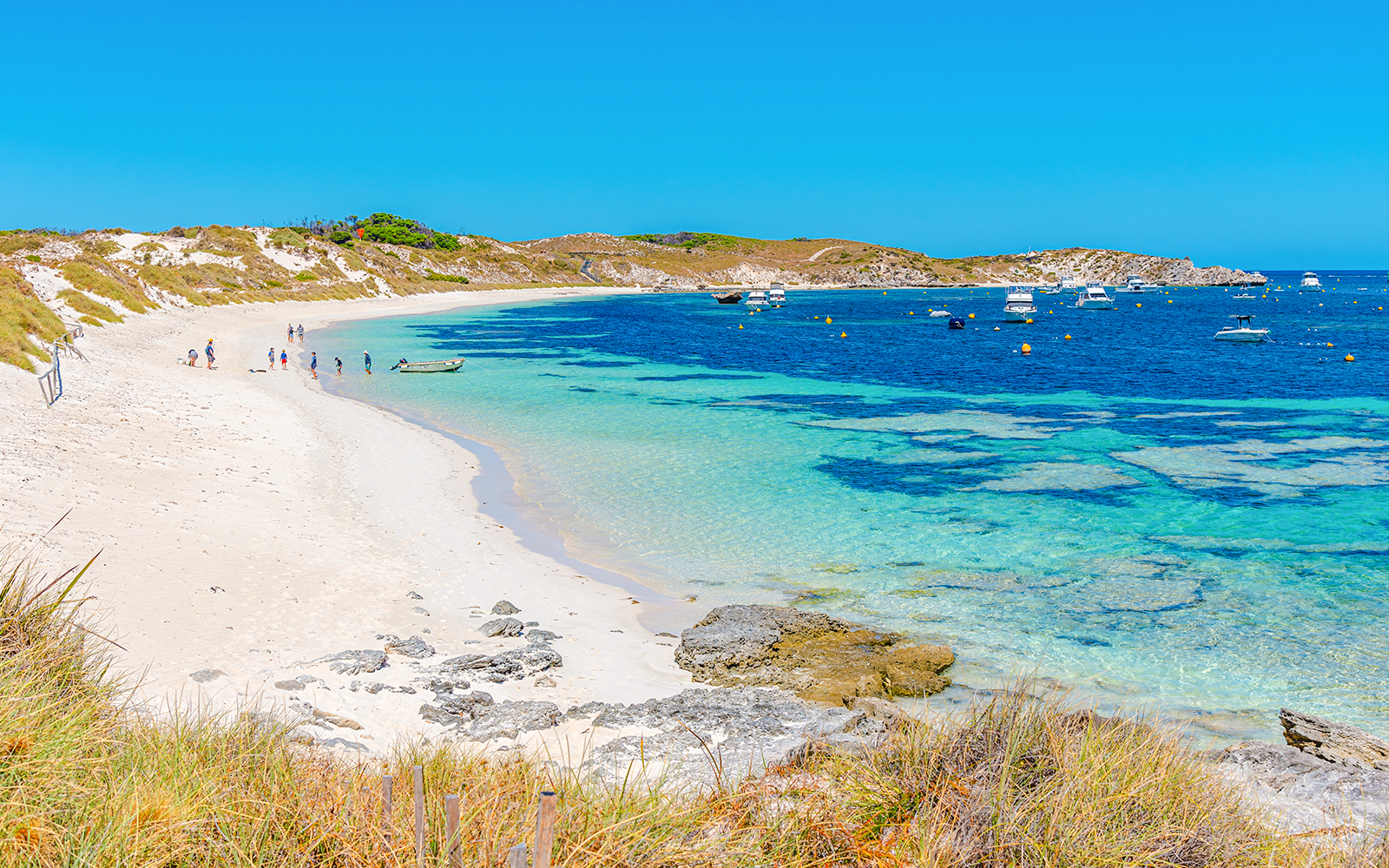Rocky bay at Rottnest Island with boats and people on the sandy beach.