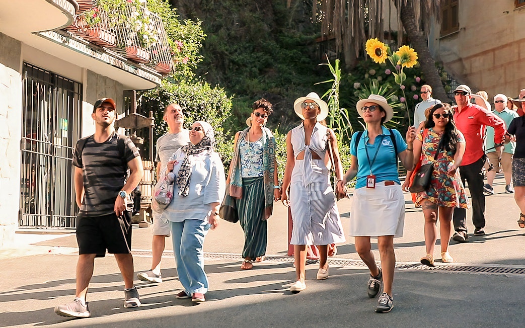 Tour group exploring Cinque Terre village street on a sunny day.