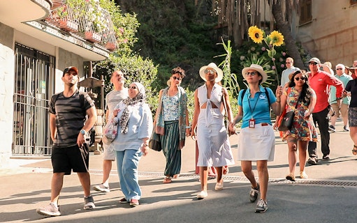 Tour group exploring Cinque Terre village street on a sunny day.