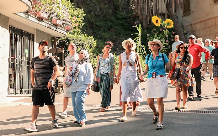 Tour group exploring Cinque Terre village street on a sunny day.
