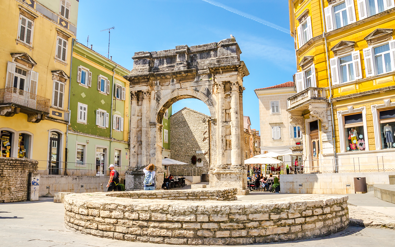 Triumphal arch and square in Pula, Croatia, with colorful buildings and people walking.
