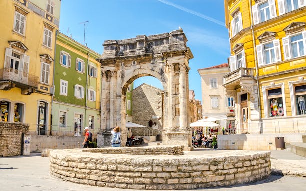 Triumphal arch and square in Pula, Croatia, with colorful buildings and people walking.