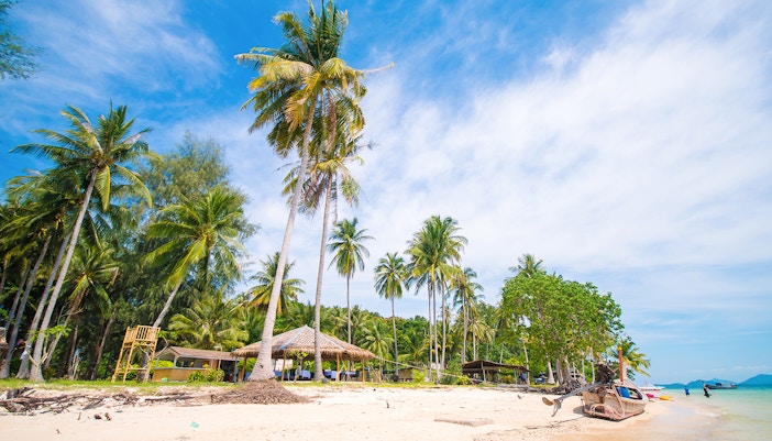 Naka Noi Island beach with palm trees and boats, Phuket, Thailand.
