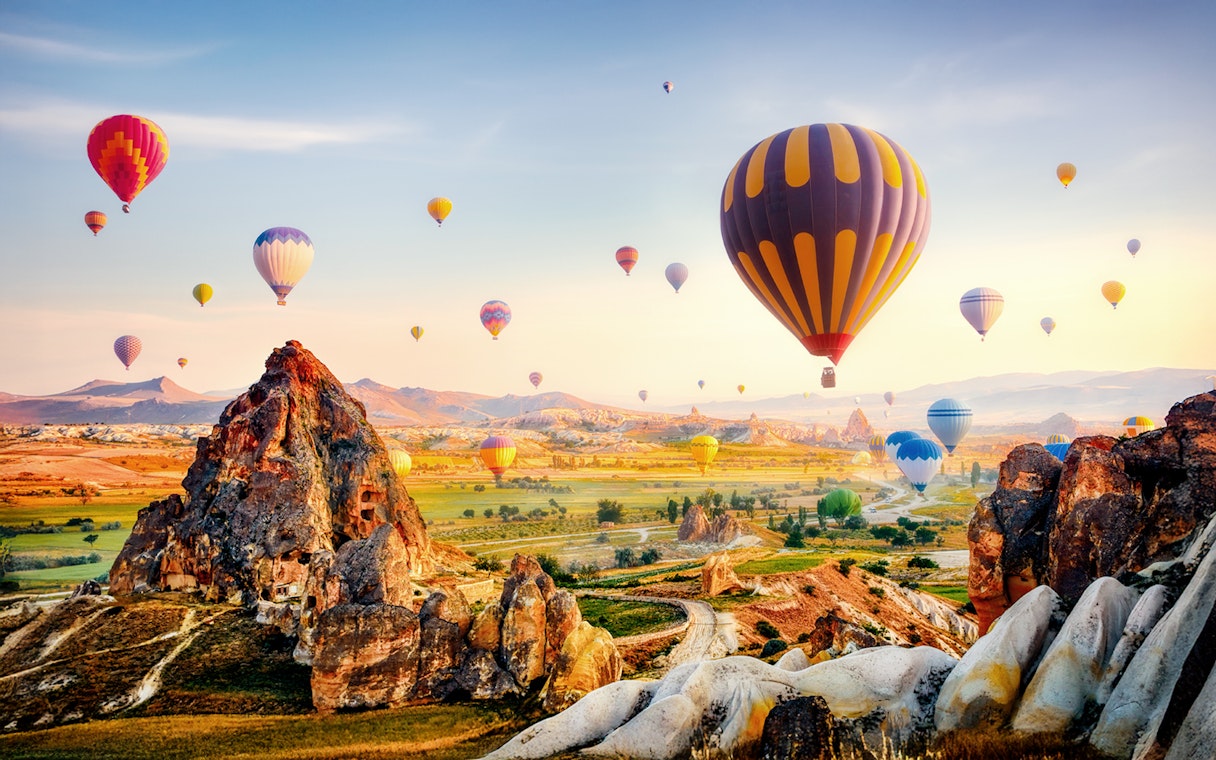 Cappadocia hot air balloons over rock formations and valleys at sunrise, Turkey.