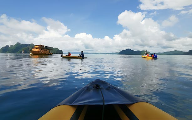 Kayakers paddling near a boat in Phang Nga Bay during a sunset cruise.