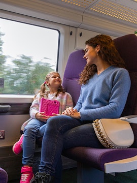 Mother and daughter on train from Heathrow Airport, child holding tablet.