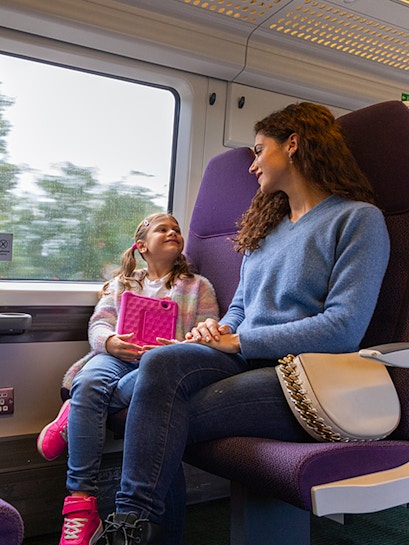 Mother and daughter on train from Heathrow Airport, child holding tablet.