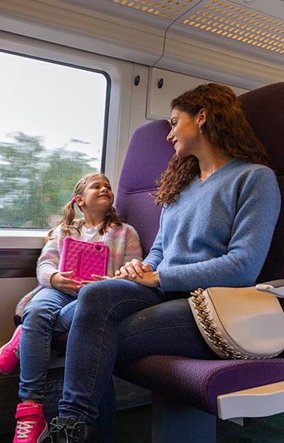 Mother and daughter on train from Heathrow Airport, child holding tablet.