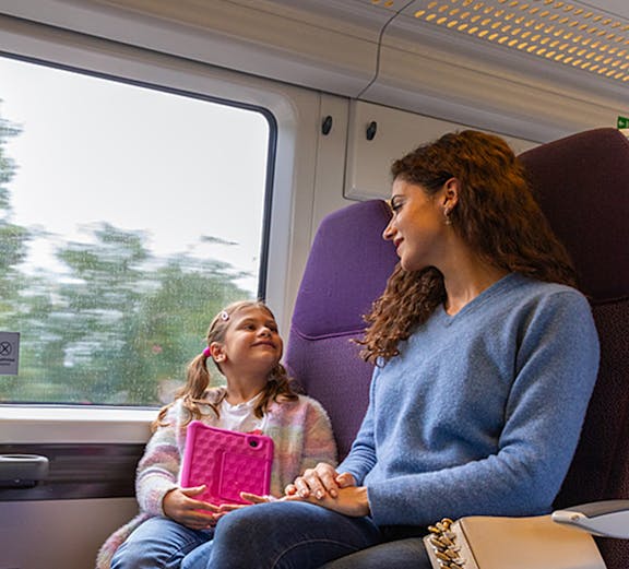 Mother and daughter on train from Heathrow Airport, child holding tablet.