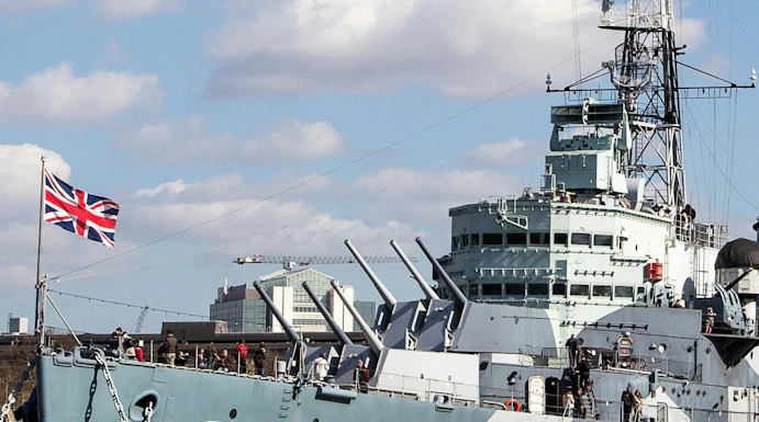 HMS Belfast moored on the River Thames in London with visitors on deck.
