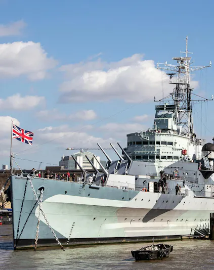 HMS Belfast moored on the River Thames in London with visitors on deck.