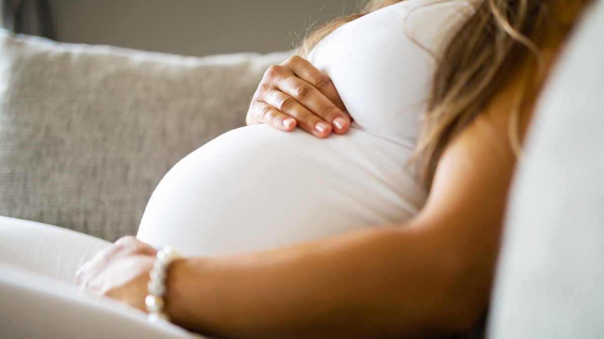 Pregnant woman resting on a couch, hand on belly.