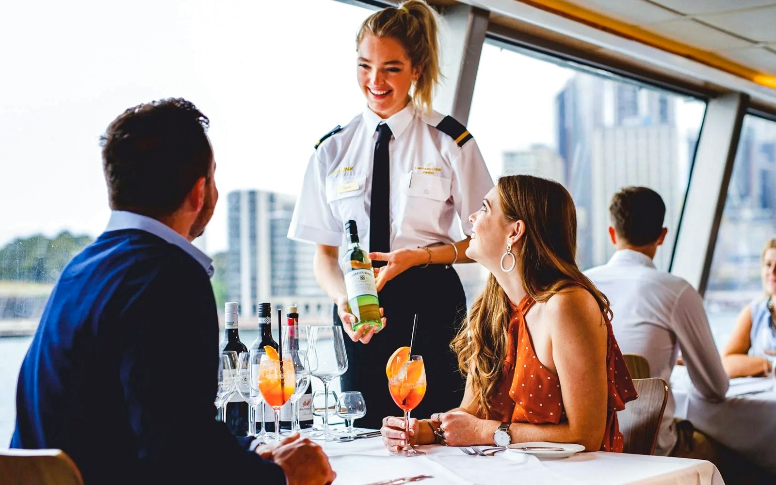 Server attending to a couple on a lunch cruise with Sydney Harbour Bridge in the background.