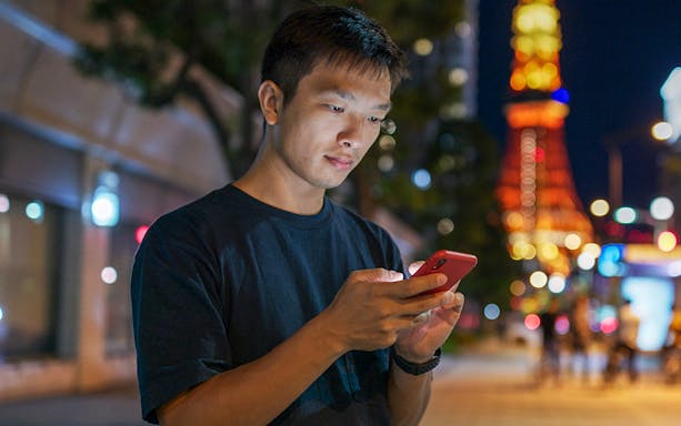 Man using a cellphone with Tokyo Tower illuminated in the background.