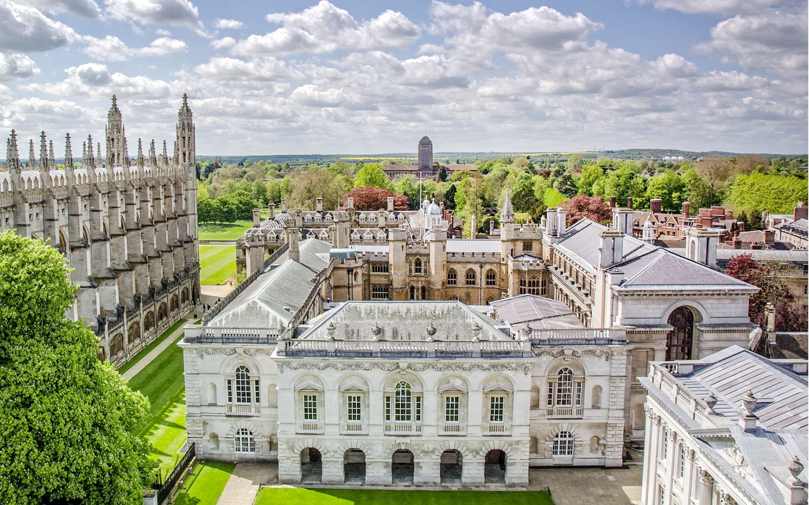 Aerial view of Cambridge University buildings and green lawns on a sunny day.