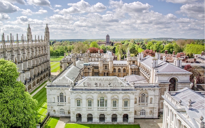 Aerial view of Cambridge University buildings and green lawns on a sunny day.