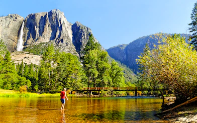 Person wading in Merced River with Yosemite Falls in background, Yosemite National Park, California.