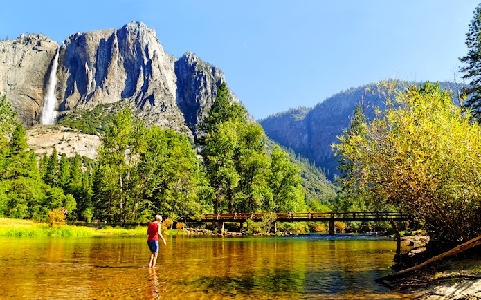 Person wading in Merced River with Yosemite Falls in background, Yosemite National Park, California.