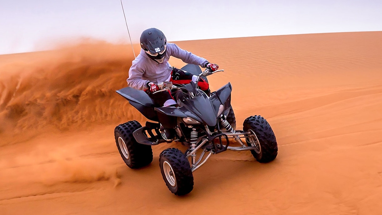 Person riding an ATV on red desert dunes during Evening Red Dune Desert Safari.