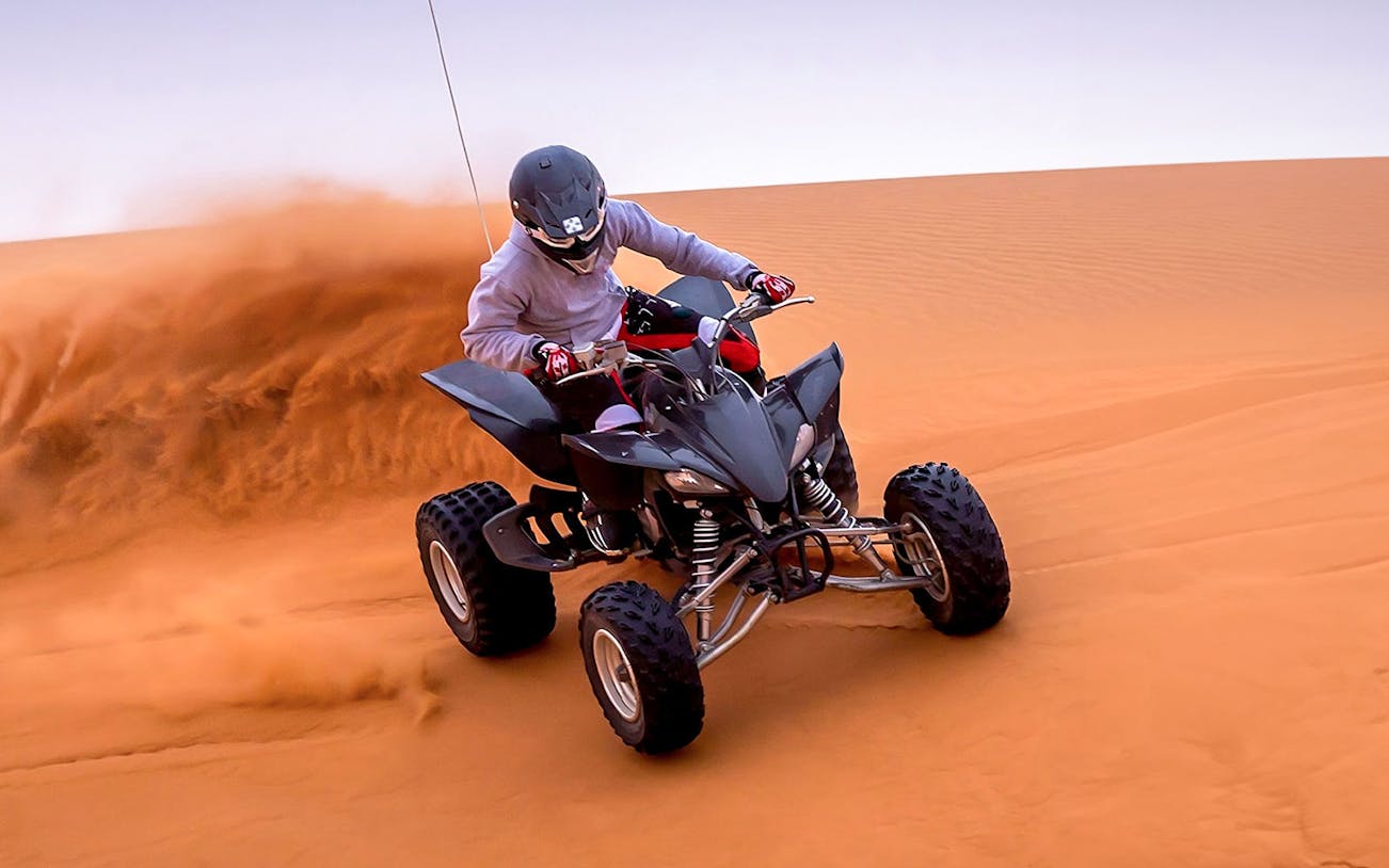 Person riding an ATV on red desert dunes during Evening Red Dune Desert Safari.
