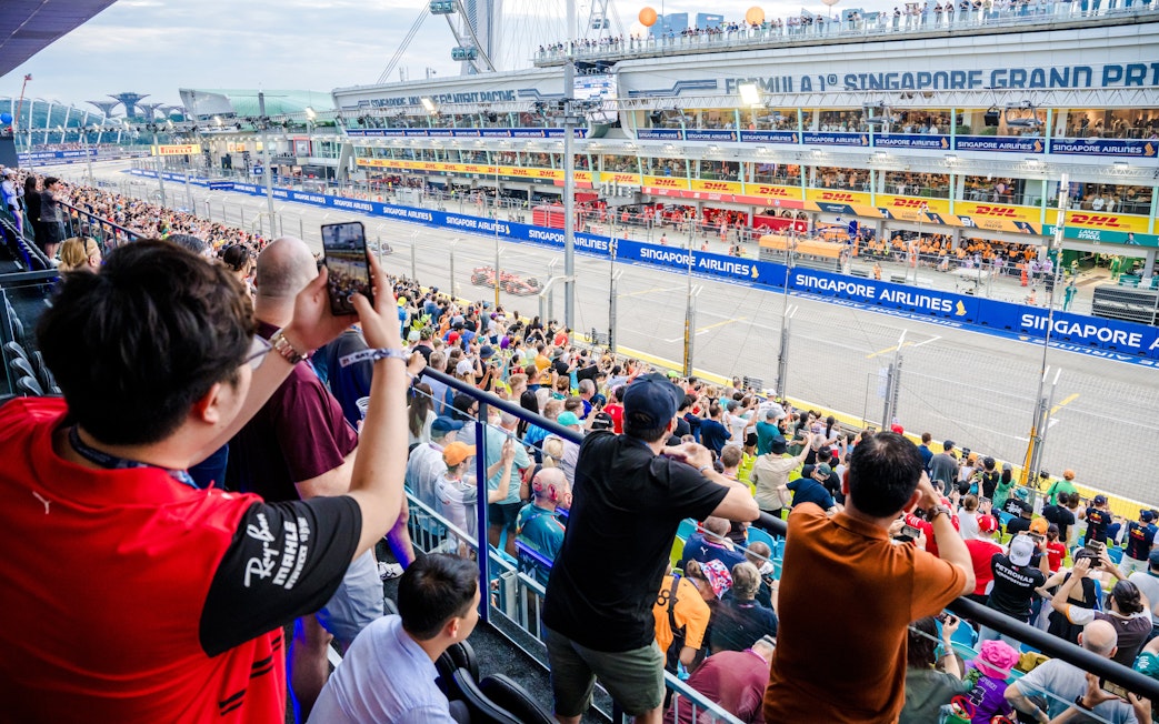 Crowd watching the Singapore Grand Prix race from the stands, capturing the vibrant atmosphere.