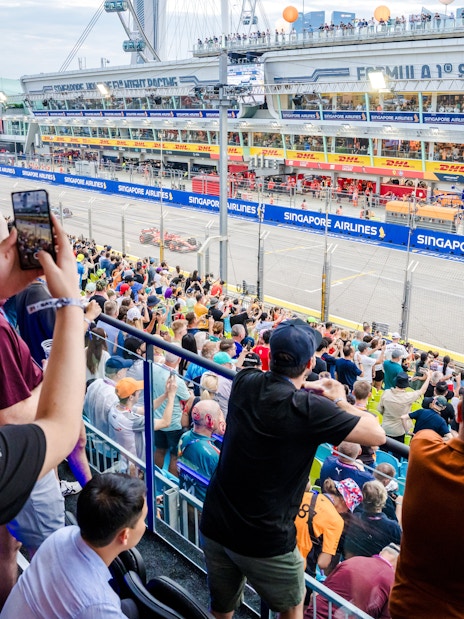 Crowd watching the Singapore Grand Prix race from the stands, capturing the vibrant atmosphere.