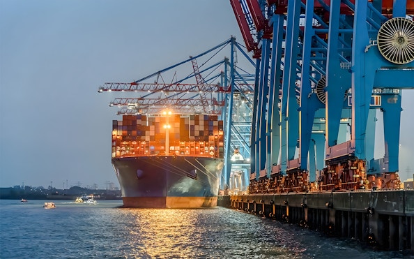 Container ship docked at illuminated harbor cranes during evening Grand Harbor cruise.