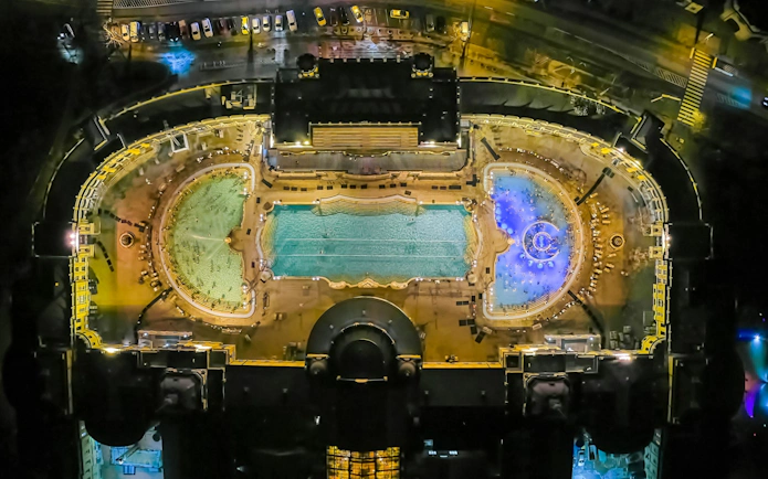Aerial view of Szechenyi Thermal Bath in Budapest at night, showcasing illuminated pools.