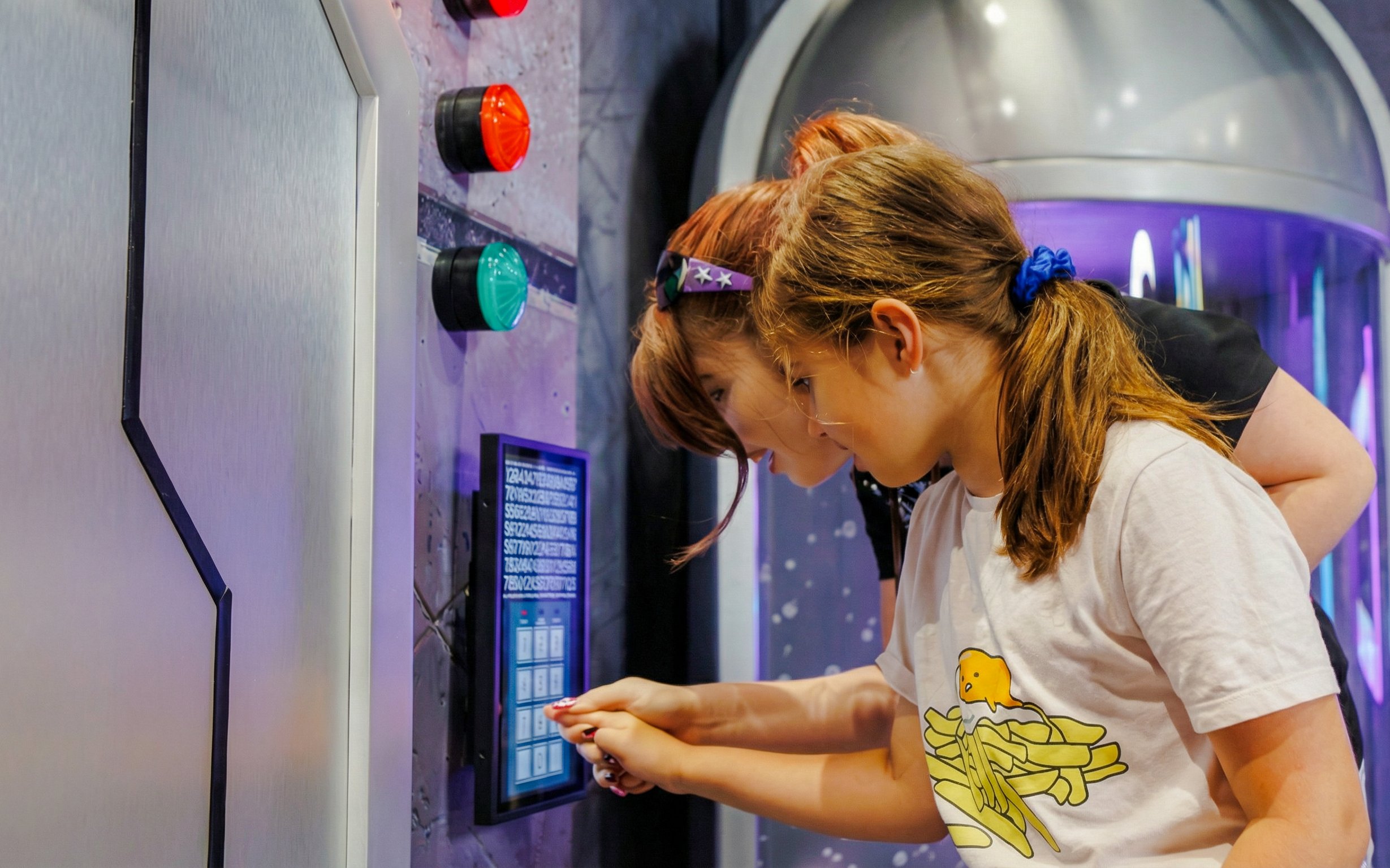 Children interacting with an illusion exhibit at TRICKD, featuring colorful buttons and a digital display.