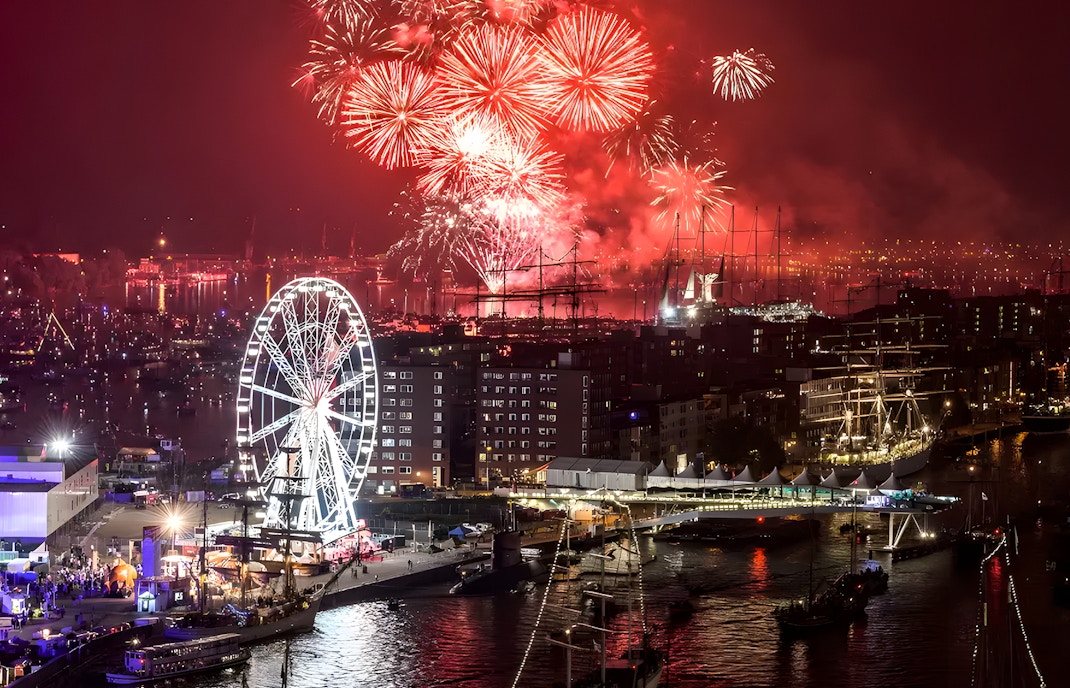 Fireworks over Amsterdam harbor during Sail Amsterdam event with ferris wheel and ships.